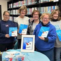 5 smiling ladies holding up their snowman paintings at Kewaunee Public Library