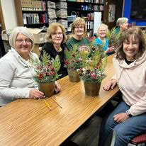 6 smiling ladies with potted floral arrangements they made at Kewaunee Public Library