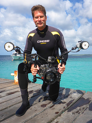 Cal Kothrade in a wetsuit, holding an underwater camera, kneeling on a dock