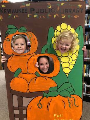 smiling and laughing library patrons posing as pumpkins and corn