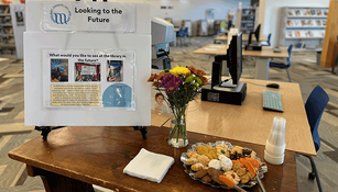 library table holding a platter of cookies, flowers, and a sign entitled 