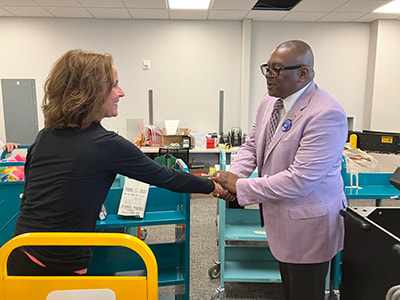 Sue Lagerman, the library's Community Engagement Manager, shakes hands with Dr. Williams in a room full of book carts.