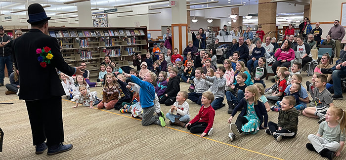 children and adults in library watching magician perform