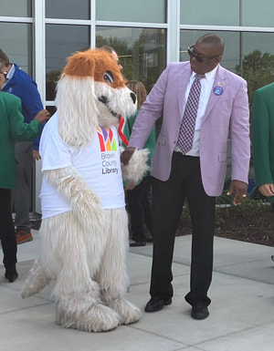 Dr. Williams is holding hands with Rover Reader (someone in a dog costume and wearing a Brown County Library T-shirt).