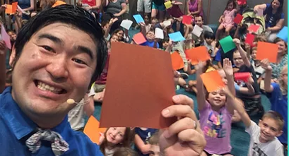 smiling performer & children holding origami paper